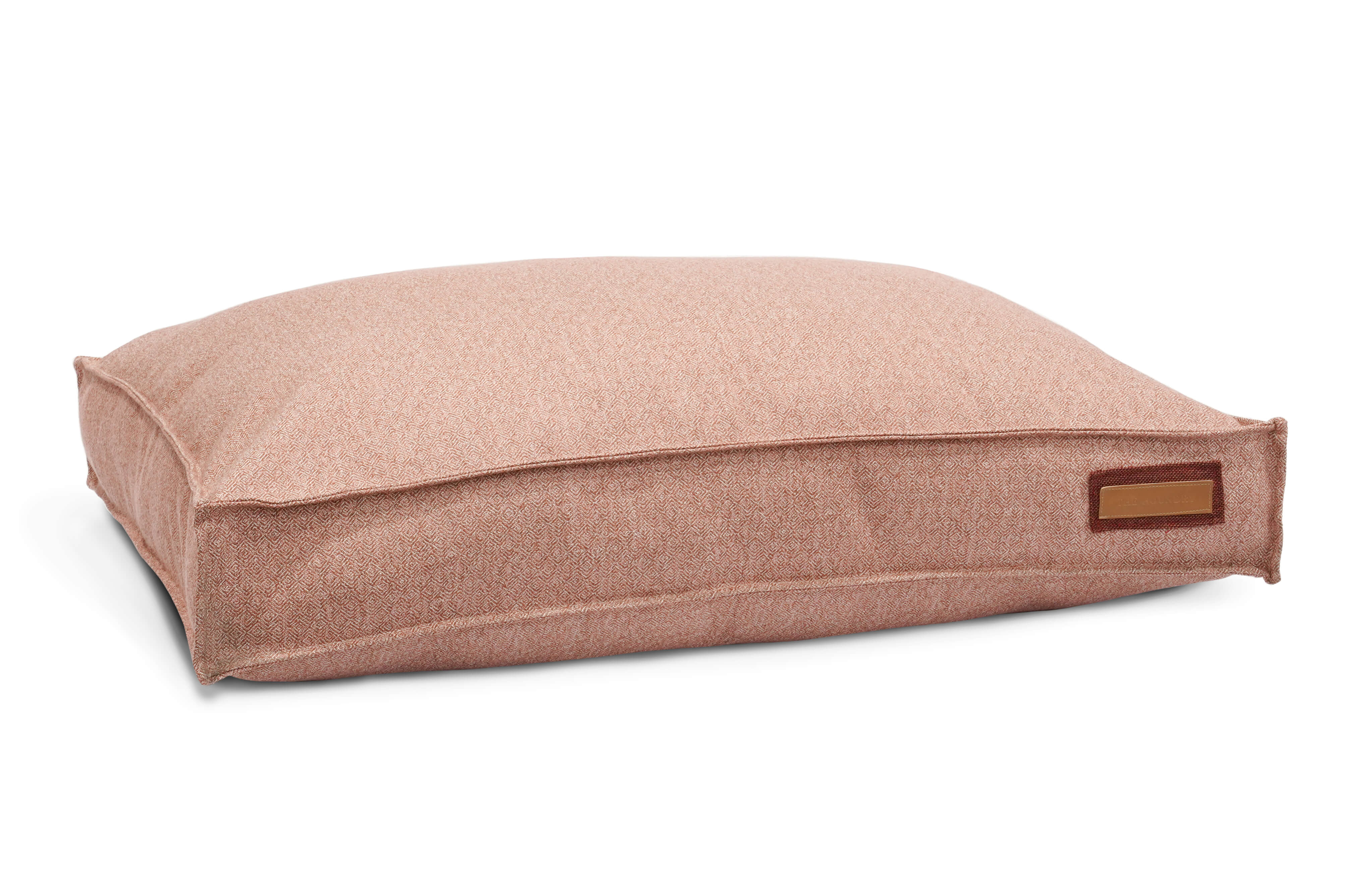 The Lounger Pet Bed in Pittie Pink features a textured surface with a repeating geometric pattern in shades of red and white, reminiscent of intricate woven or embroidered fabric, crafted from Sunbrella fabric made using recycled plastic water bottles.