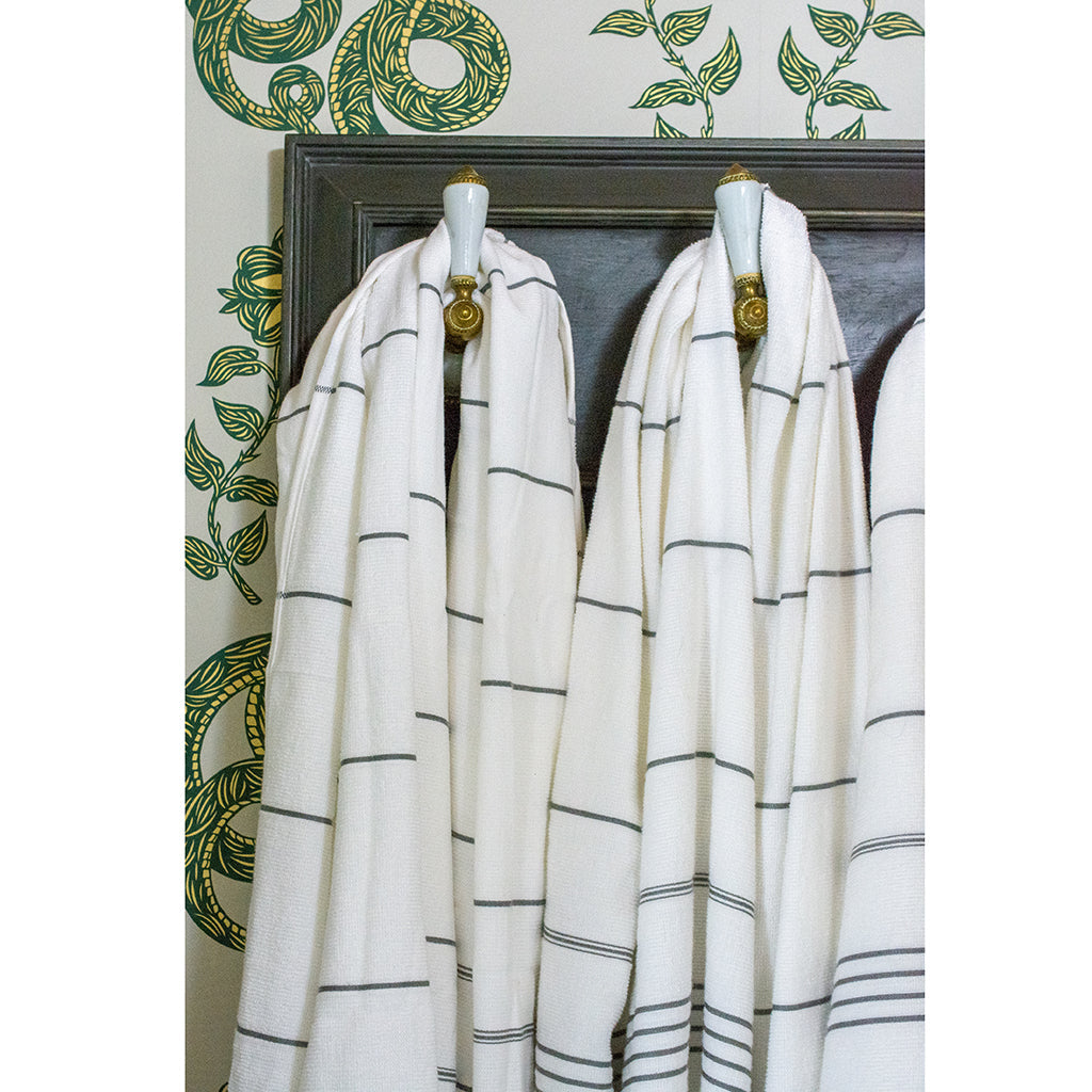 The Classic Terry Turkish Towel is a handmade white towel featuring horizontal gray stripes and fringed edges, ideal for enhancing the elegance of your bath collection.