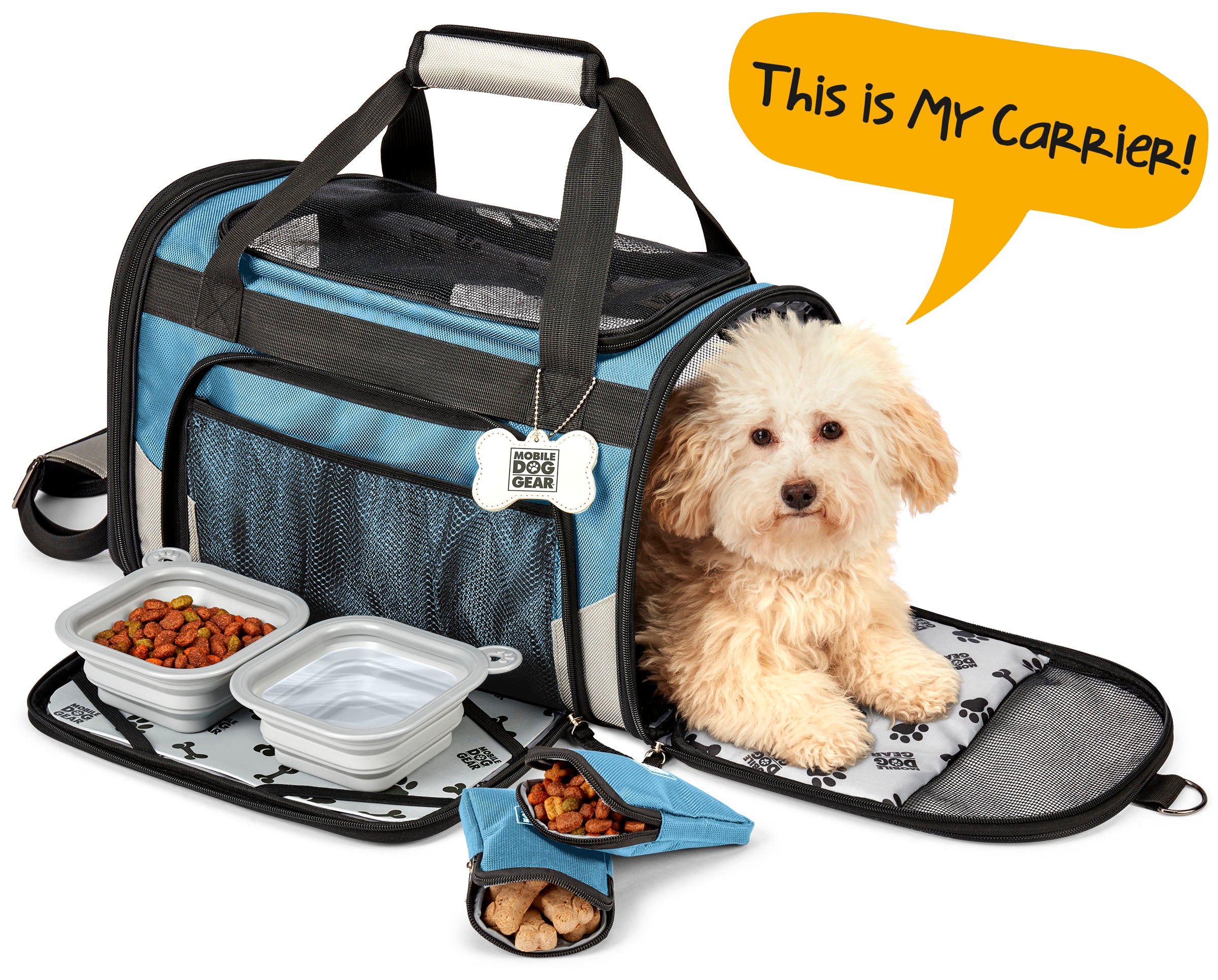 A small dog sits comfortably in a Mobile Dog Gear Pet Carrier Plus, complete with food and water bowls nearby. A speech bubble above says, "This is MY carrier!