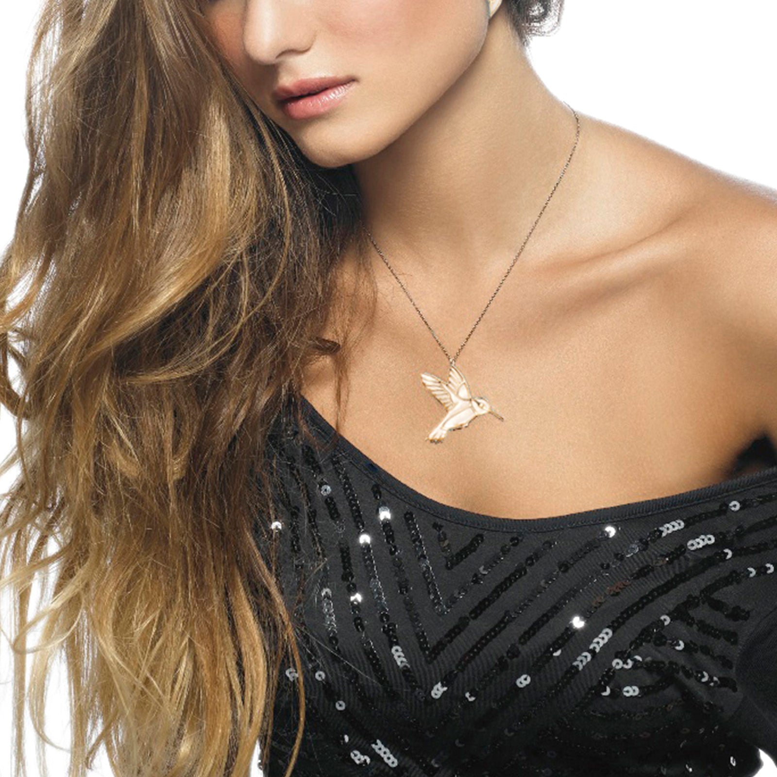 A woman wearing a sequined black top and a Gold Plated Sterling Silver Hummingbird Necklace Pendant, showing her shoulder and long, wavy hair.