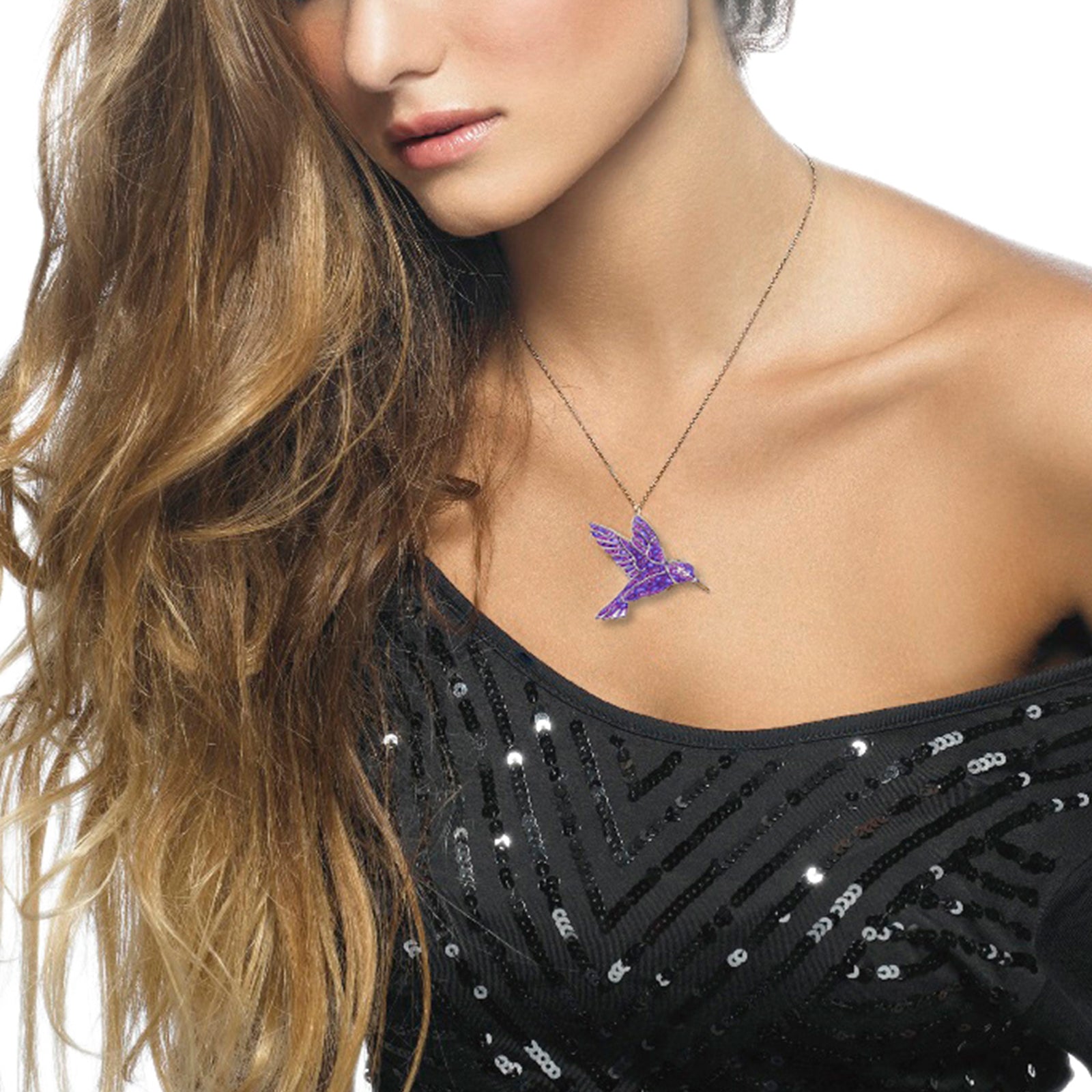 A woman wearing a sequined black top and a Gold Plated Sterling Silver Hummingbird Necklace Pendant, showing her shoulder and long, wavy hair.