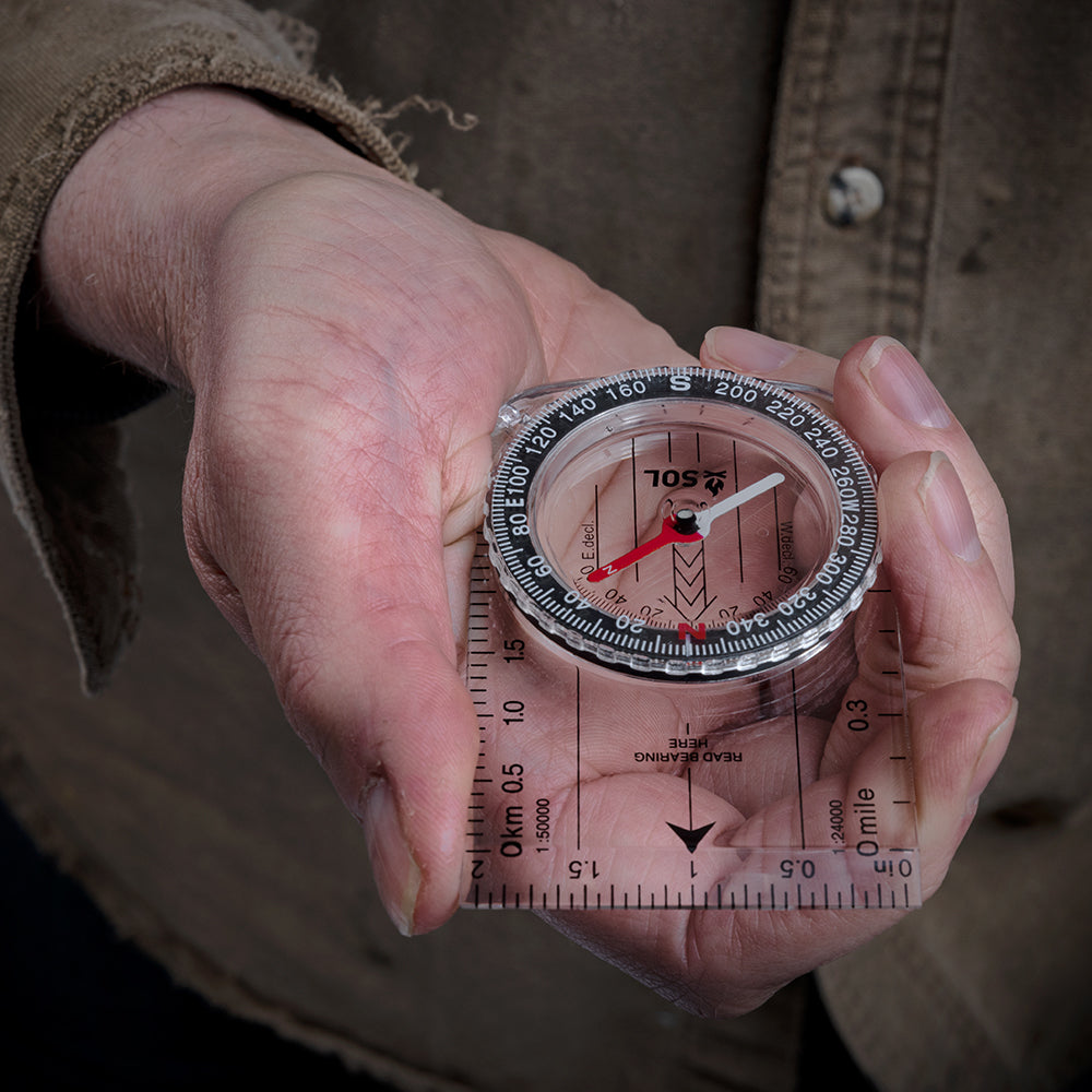 A S.O.L. Survive Outdoors Longer Map Compass with a cord attached to it.