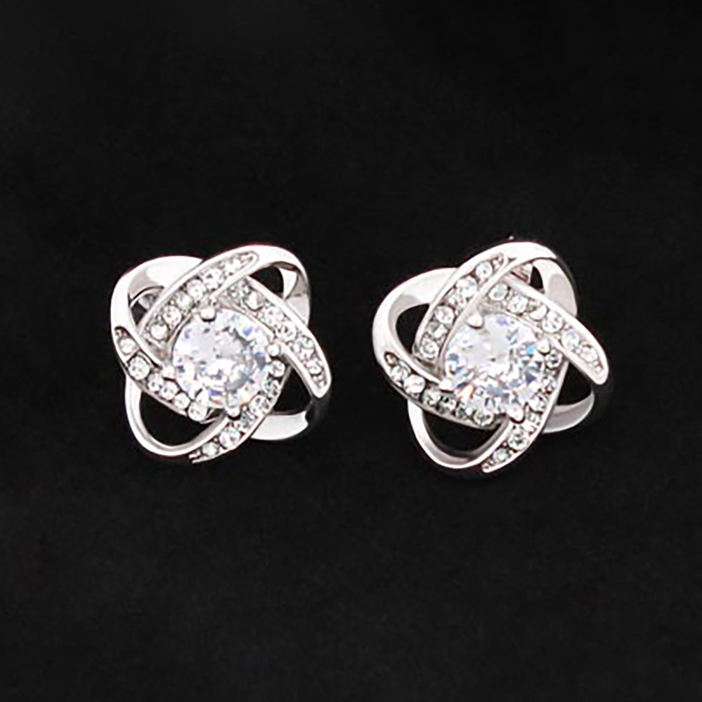 A pair of 14K white gold Love Knot Stud Earrings adorned with small diamonds and central larger stones, displayed against a black background.
