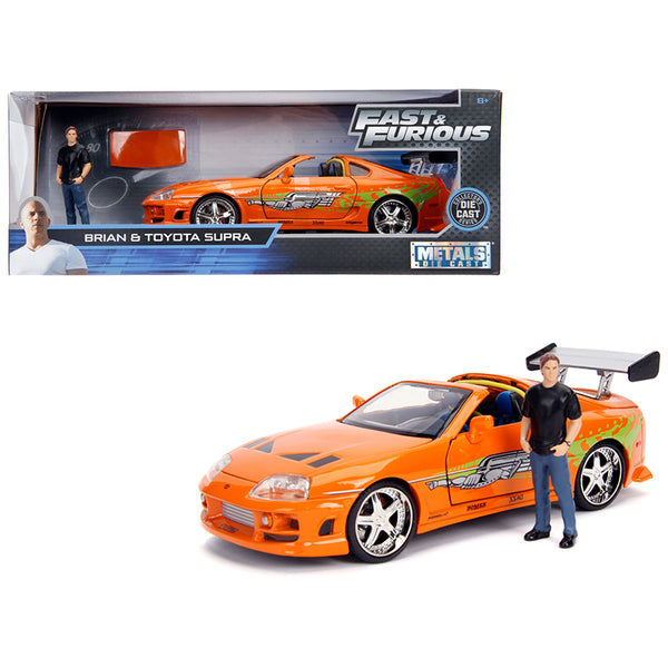 A Toyota Supra Orange Metallic with Brian Diecast Figurine "Fast & Furious" Movie 1/24 Diecast Model Car by Jada with a man standing next to it.