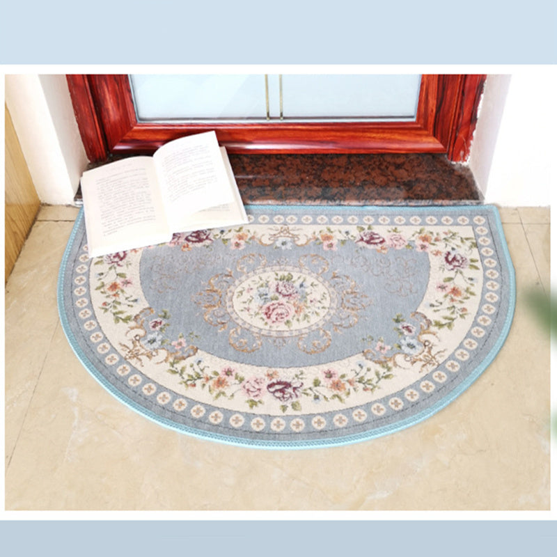 A European Style Semicircle Entrance Carpet with floral designs and a pastel color scheme on a wooden floor, next to a stool and a pair of slippers.