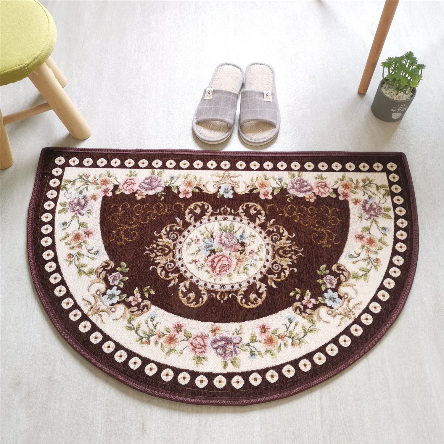 A European Style Semicircle Entrance Carpet with floral designs and a pastel color scheme on a wooden floor, next to a stool and a pair of slippers.