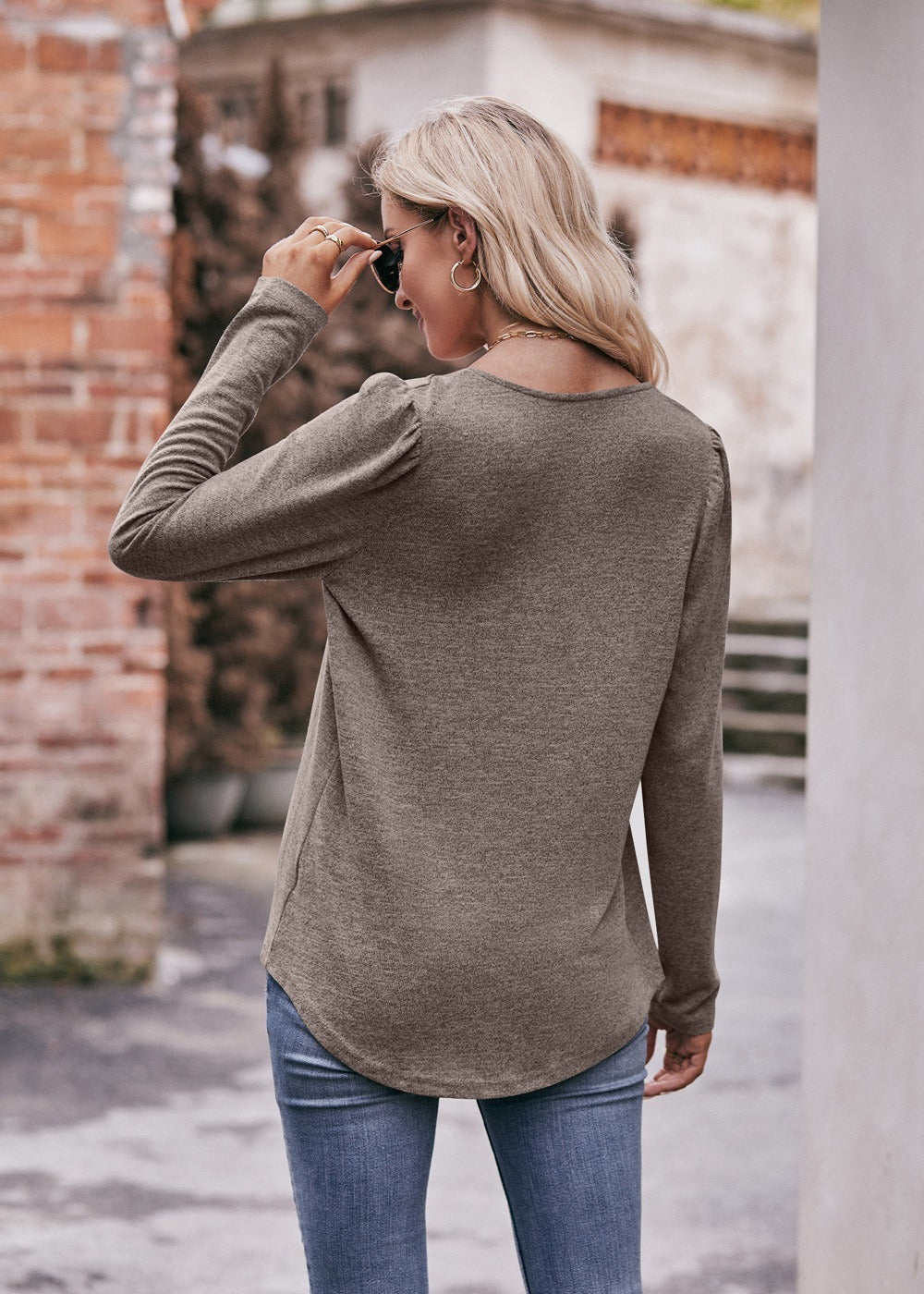 Woman in a Women Long Sleeve Shirt Lightweight Crew Neck Casual Tunic Top 8 Colors and skinny jeans, wearing sunglasses and a white hat, carrying a beige shoulder bag, standing in a quaint street.