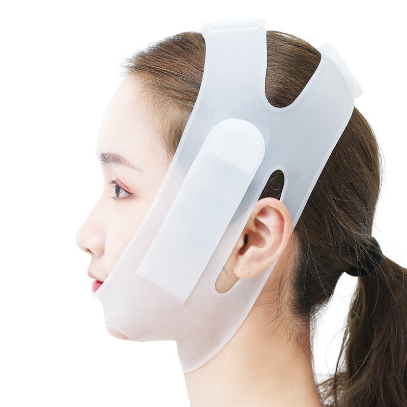 A person wearing a Women Chin Cheek Silicone Face Slimming Bandage Lift Up Belt V Line Face Shaper Facial Anti Wrinkle Strap Skin Care Beauty Tools that covers the chin and wraps around the back of the head. Their hand gently touches the bandage, highlighting its intricate details.