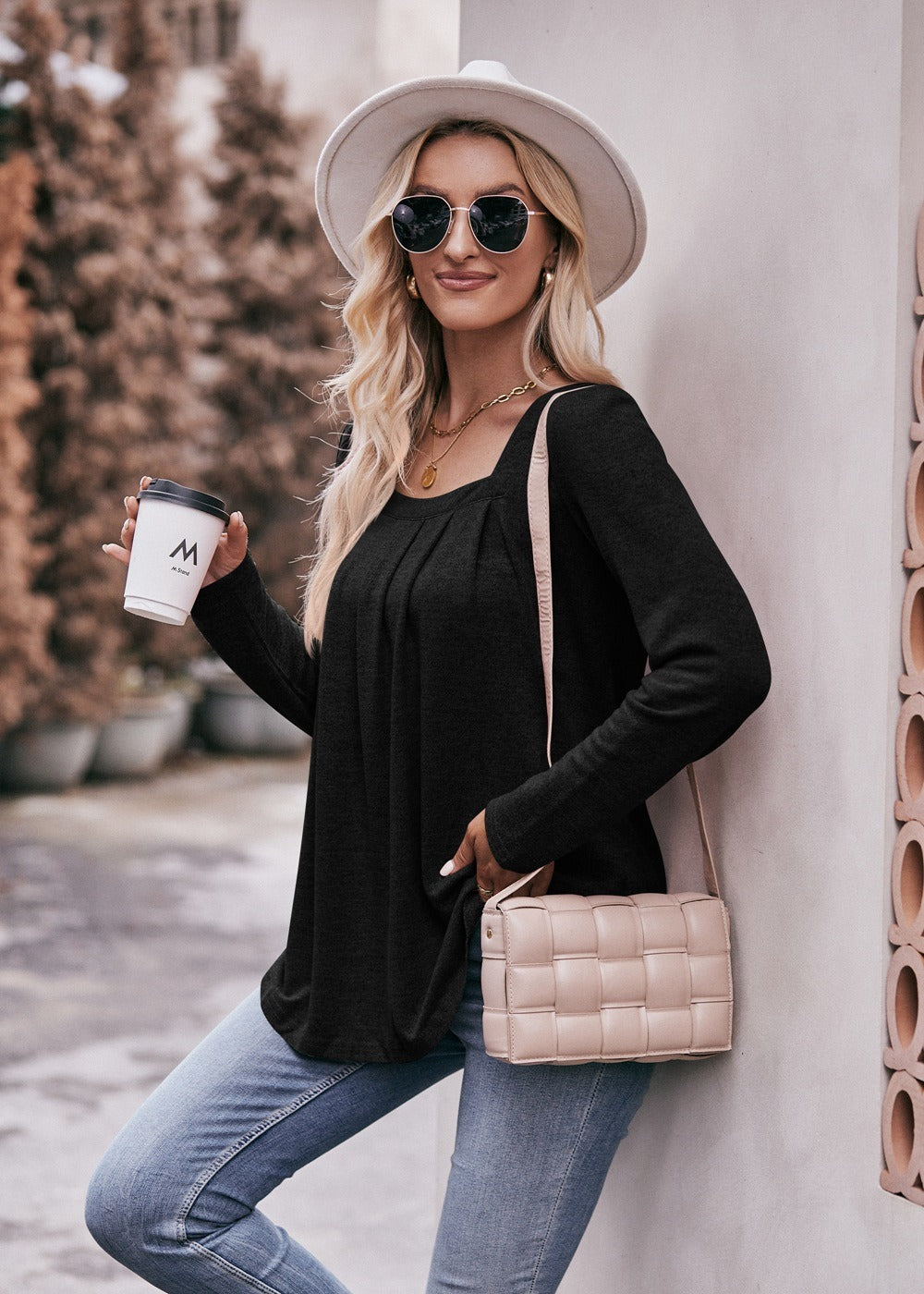 Woman in a Women Long Sleeve Shirt Lightweight Crew Neck Casual Tunic Top 8 Colors and skinny jeans, wearing sunglasses and a white hat, carrying a beige shoulder bag, standing in a quaint street.