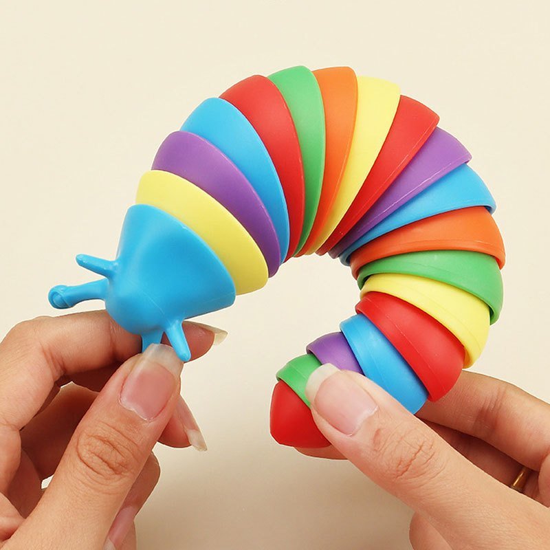 A colorful silicone Fidget Slug toy designed for educational purposes, in a rainbow design, held in a person's hand with packaging visible in the background.