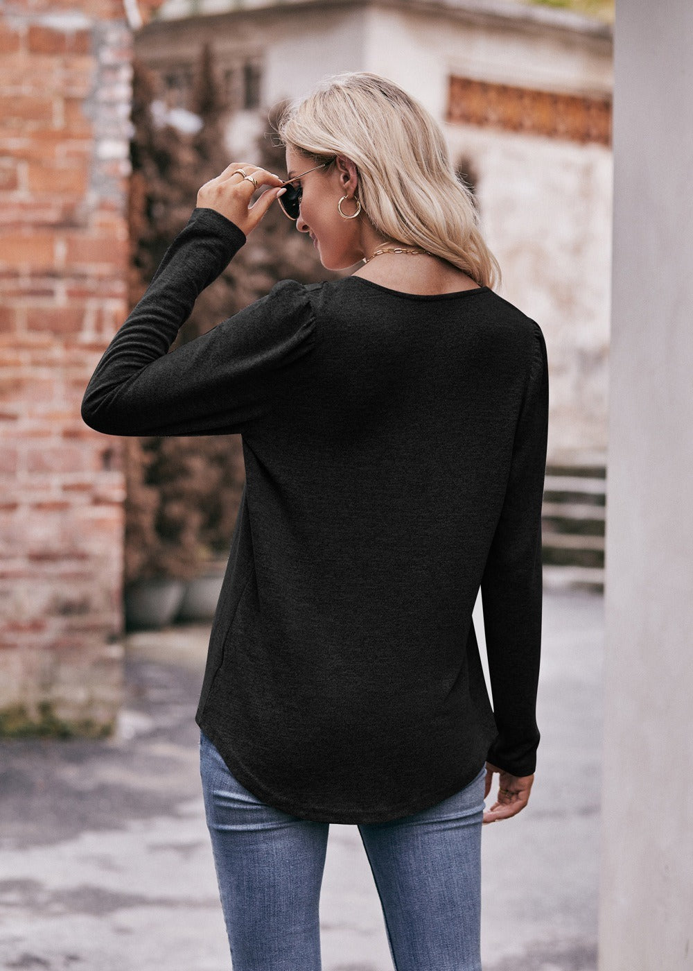 Woman in a Women Long Sleeve Shirt Lightweight Crew Neck Casual Tunic Top 8 Colors and skinny jeans, wearing sunglasses and a white hat, carrying a beige shoulder bag, standing in a quaint street.