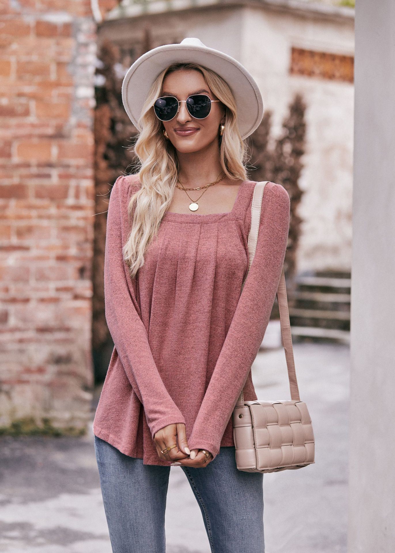 Woman in a Women Long Sleeve Shirt Lightweight Crew Neck Casual Tunic Top 8 Colors and skinny jeans, wearing sunglasses and a white hat, carrying a beige shoulder bag, standing in a quaint street.