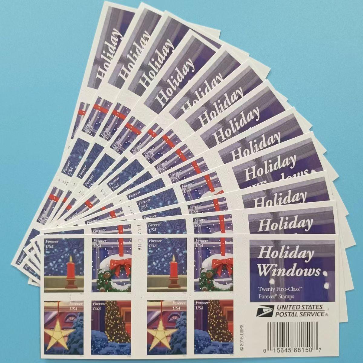 A booklet of U.S. postage stamps featuring various patriotic designs next to a Holiday Windows 2016 - 5 Booklets / 100 Pcs-themed postage label on a textured surface.