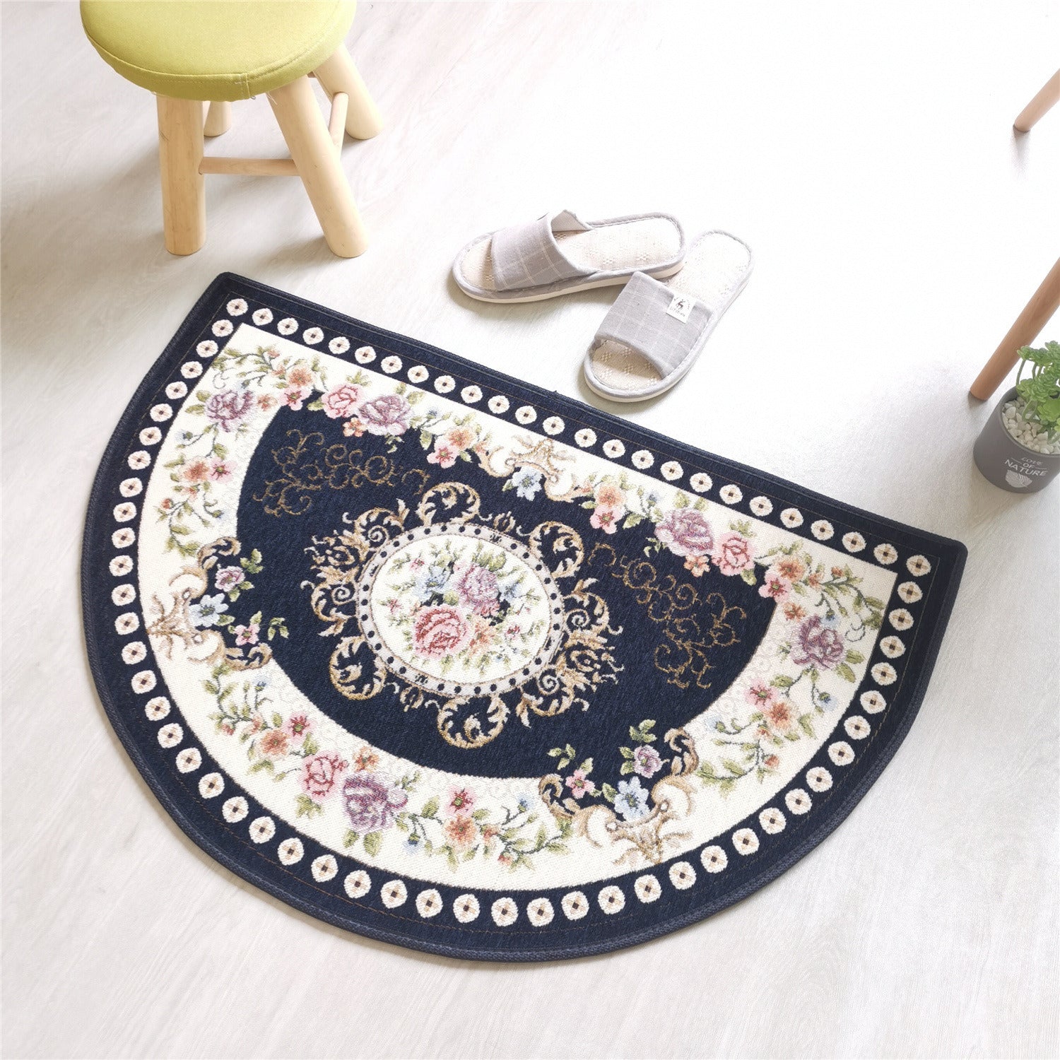 A European Style Semicircle Entrance Carpet with floral designs and a pastel color scheme on a wooden floor, next to a stool and a pair of slippers.