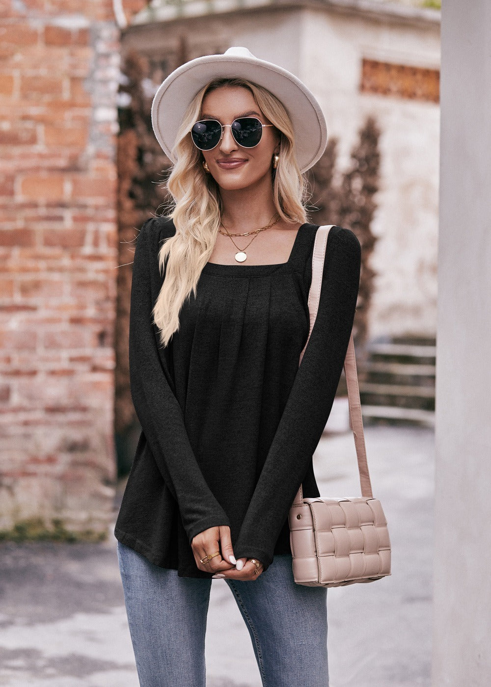 Woman in a Women Long Sleeve Shirt Lightweight Crew Neck Casual Tunic Top 8 Colors and skinny jeans, wearing sunglasses and a white hat, carrying a beige shoulder bag, standing in a quaint street.