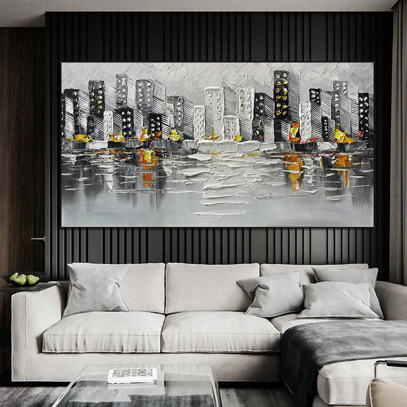 Sentence with the product name: Abstract Art White Pictures Canvas Painting of a cityscape above a green sofa, featuring gray and black buildings with yellow and orange accents, reflected on a water-like surface.