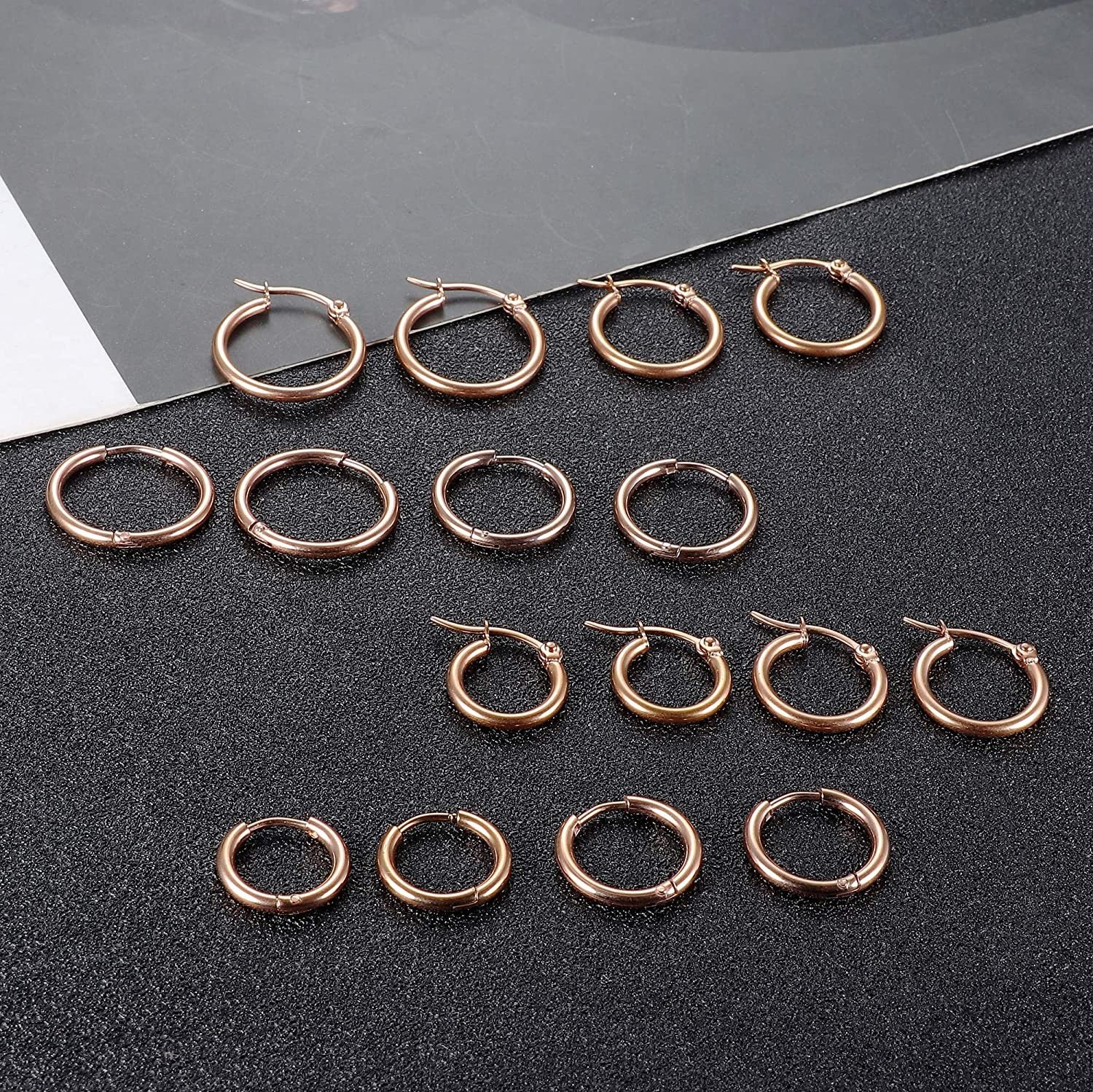 Presenting the Stainless Hoop Earrings Set for Women and Men, featuring 16 gold-plated silver-tone rounded earrings beautifully arranged in four rows. This versatile collection includes small cute huggie hoops to larger hoop earrings, making it an ideal gift for those who love to accessorize with elegance and style.