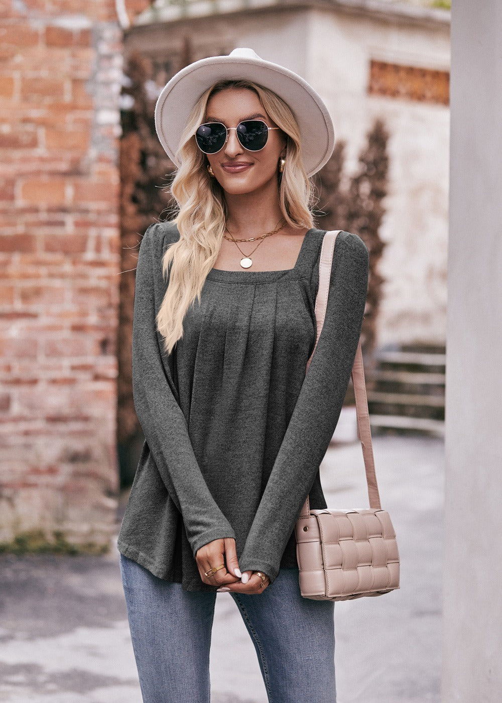 Woman in a Women Long Sleeve Shirt Lightweight Crew Neck Casual Tunic Top 8 Colors and skinny jeans, wearing sunglasses and a white hat, carrying a beige shoulder bag, standing in a quaint street.