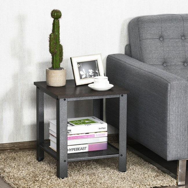 A small, Industrial End Table 2-Tier Side Table with a dark metal frame and a solid wood top, displaying a vase with flowers, a photo frame, a coffee cup, and glasses, with a storage basket on.