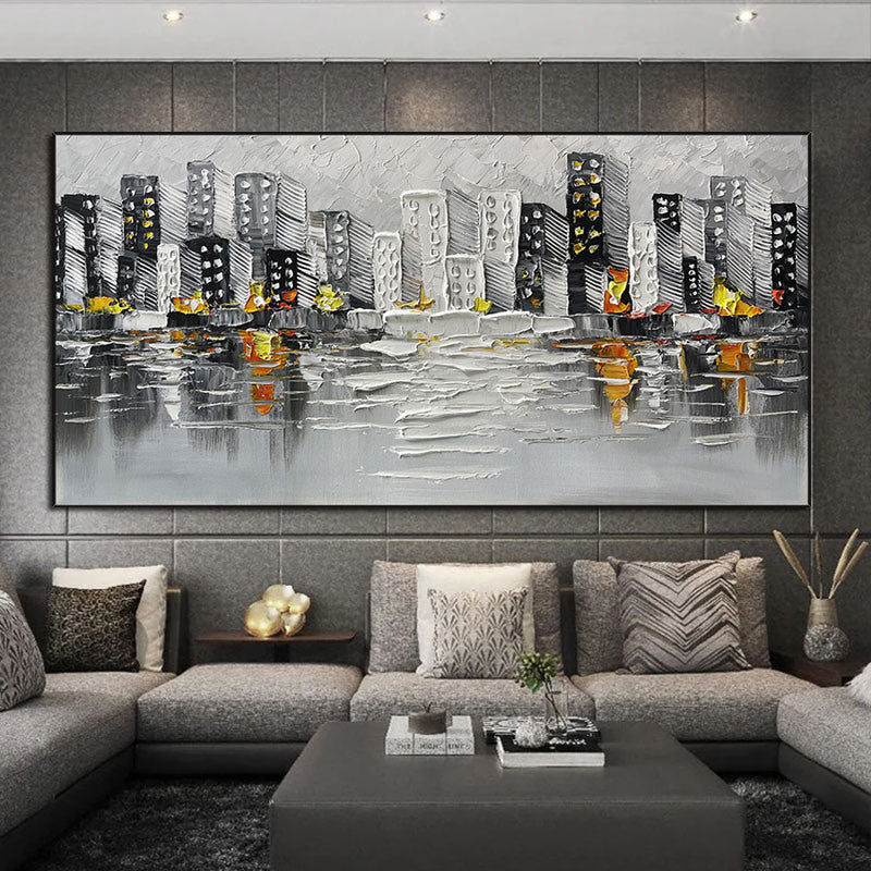 Sentence with the product name: Abstract Art White Pictures Canvas Painting of a cityscape above a green sofa, featuring gray and black buildings with yellow and orange accents, reflected on a water-like surface.