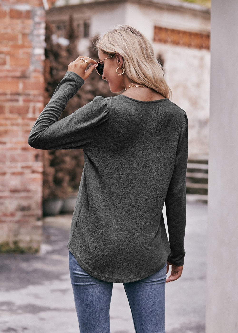 Woman in a Women Long Sleeve Shirt Lightweight Crew Neck Casual Tunic Top 8 Colors and skinny jeans, wearing sunglasses and a white hat, carrying a beige shoulder bag, standing in a quaint street.