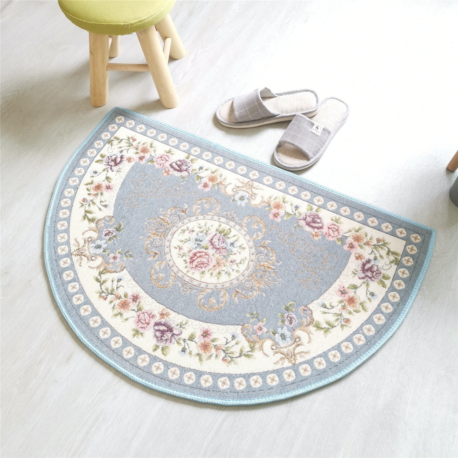 A European Style Semicircle Entrance Carpet with floral designs and a pastel color scheme on a wooden floor, next to a stool and a pair of slippers.