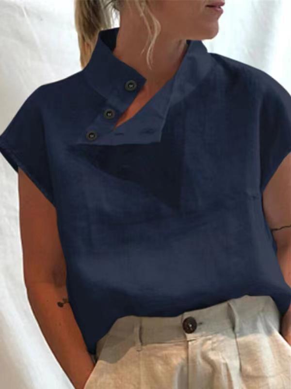 Person wearing a Stylish Blouses Summer Women Cotton Linen Short Sleeve Buttons Solid Shirt in navy blue, paired with light-colored trousers, standing against a plain backdrop.