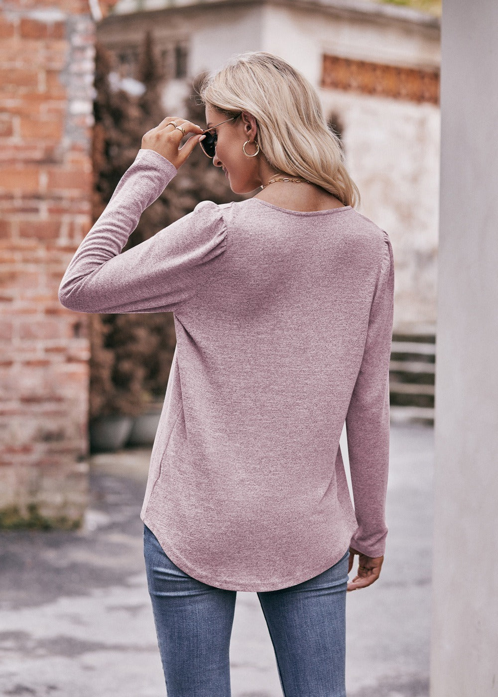 Woman in a Women Long Sleeve Shirt Lightweight Crew Neck Casual Tunic Top 8 Colors and skinny jeans, wearing sunglasses and a white hat, carrying a beige shoulder bag, standing in a quaint street.