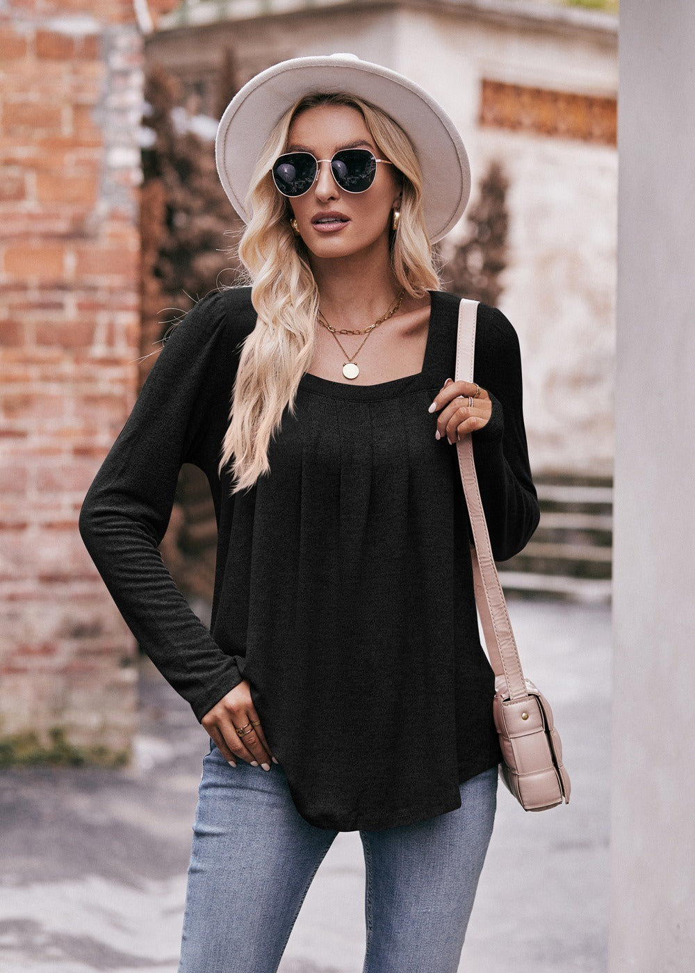 Woman in a Women Long Sleeve Shirt Lightweight Crew Neck Casual Tunic Top 8 Colors and skinny jeans, wearing sunglasses and a white hat, carrying a beige shoulder bag, standing in a quaint street.