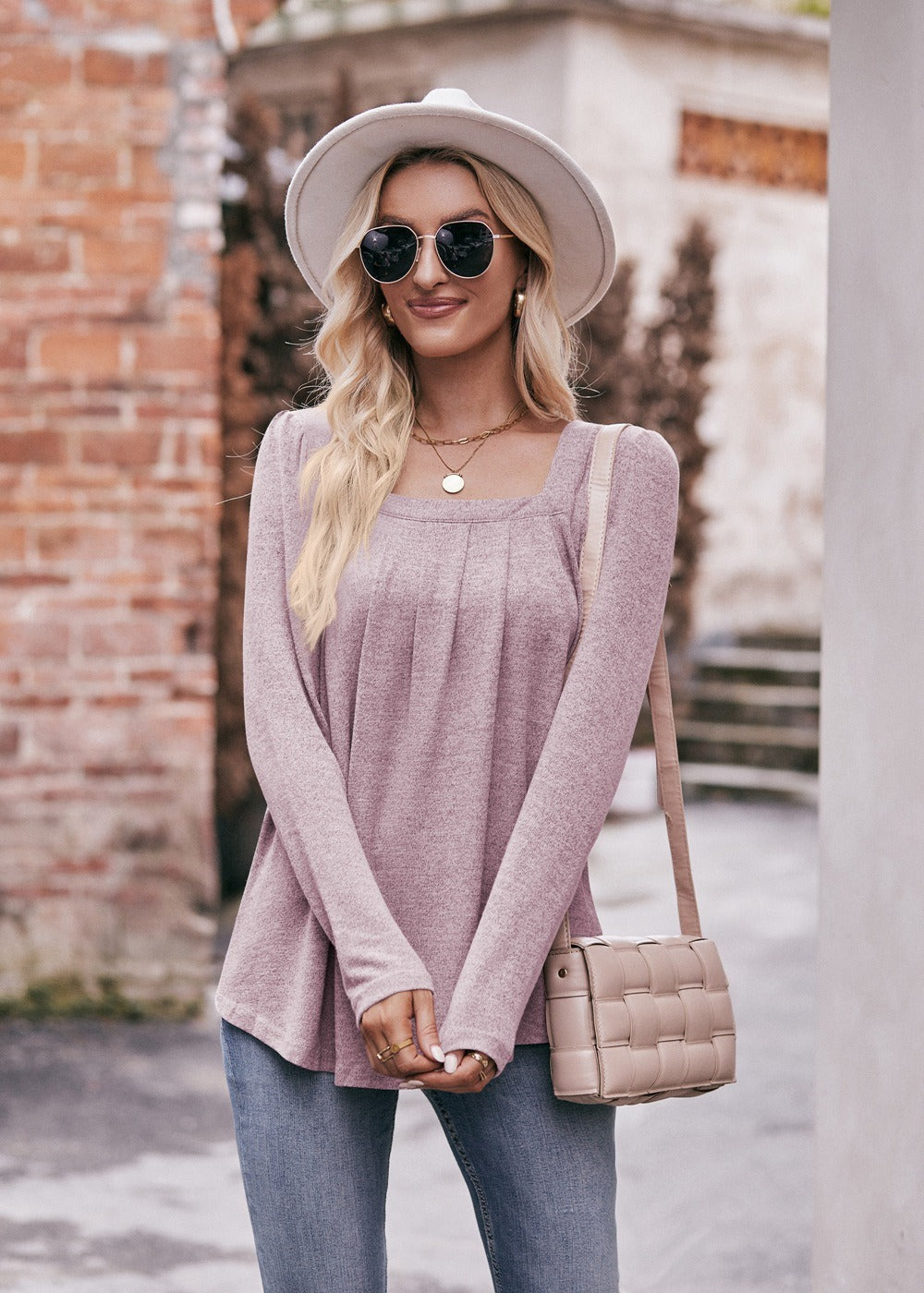 Woman in a Women Long Sleeve Shirt Lightweight Crew Neck Casual Tunic Top 8 Colors and skinny jeans, wearing sunglasses and a white hat, carrying a beige shoulder bag, standing in a quaint street.