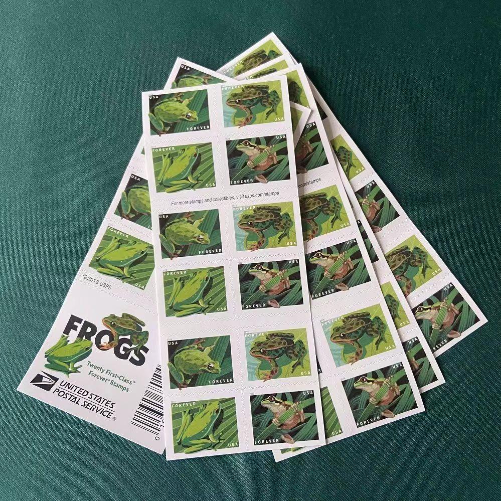 A stack of Frogs 2019 - 5 Booklets / 100 Pcs postage stamps featuring various green frogs illustrations scattered on a white surface, showcasing details of the frogs dating back to 2019.