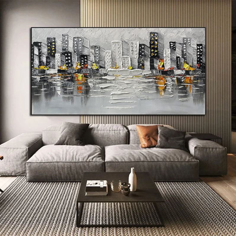 Sentence with the product name: Abstract Art White Pictures Canvas Painting of a cityscape above a green sofa, featuring gray and black buildings with yellow and orange accents, reflected on a water-like surface.