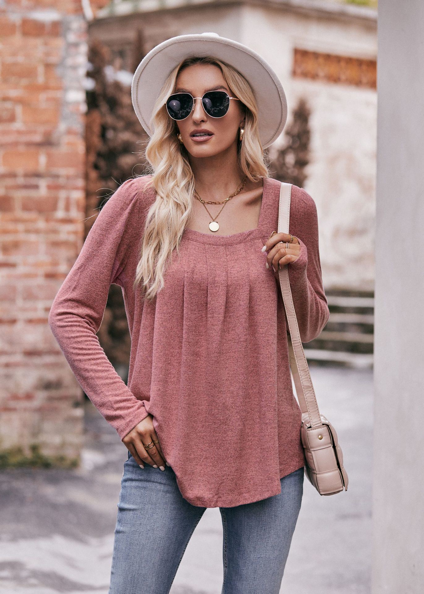 Woman in a Women Long Sleeve Shirt Lightweight Crew Neck Casual Tunic Top 8 Colors and skinny jeans, wearing sunglasses and a white hat, carrying a beige shoulder bag, standing in a quaint street.