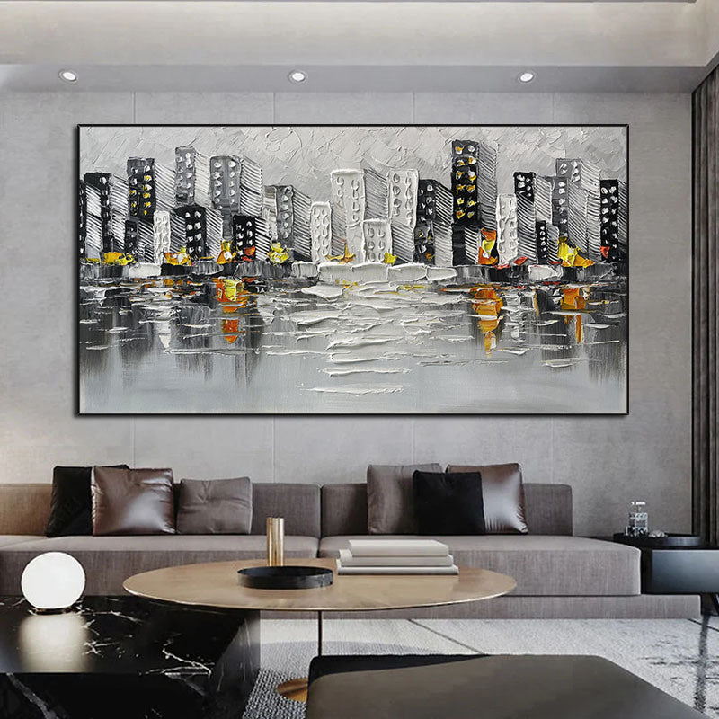 Sentence with the product name: Abstract Art White Pictures Canvas Painting of a cityscape above a green sofa, featuring gray and black buildings with yellow and orange accents, reflected on a water-like surface.