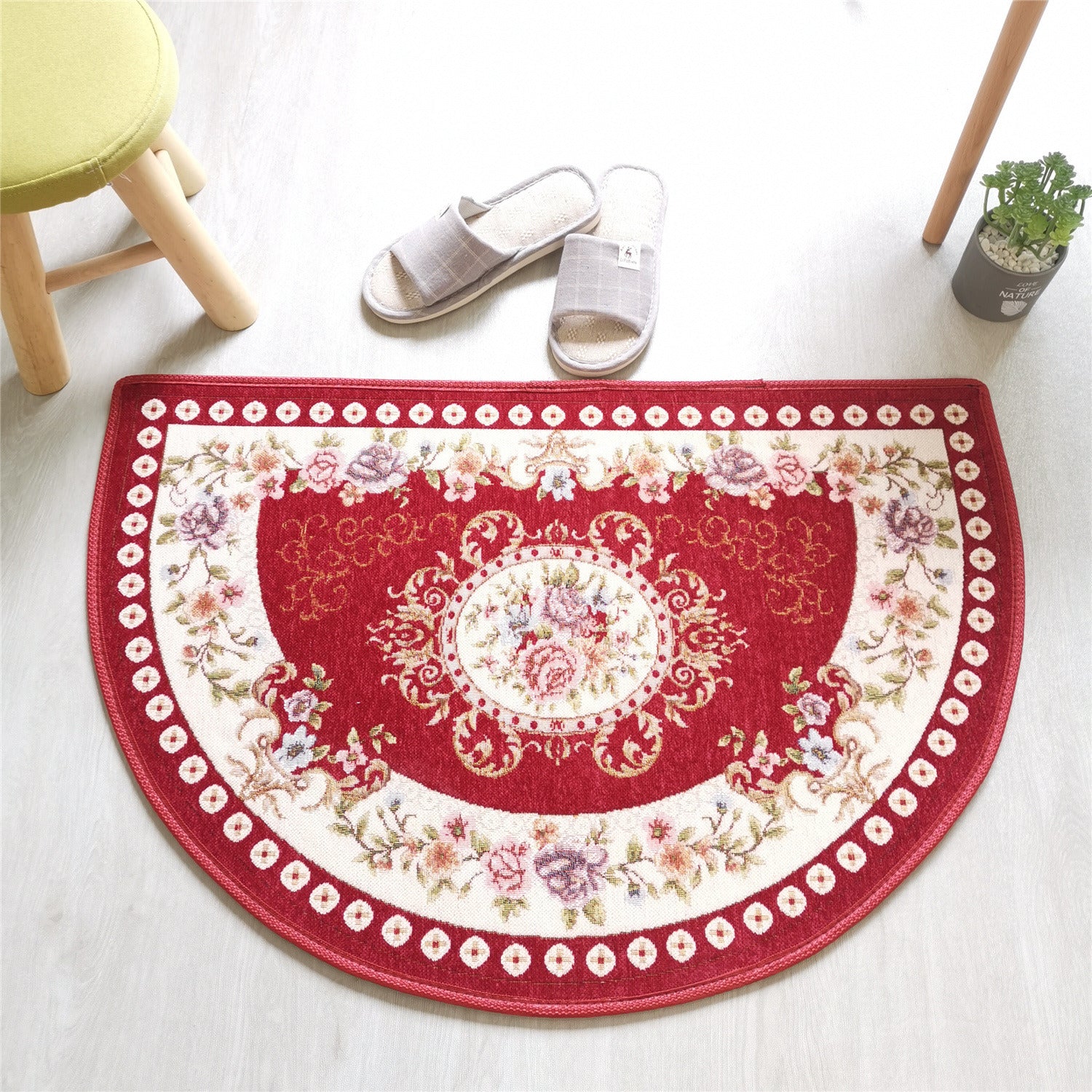 A European Style Semicircle Entrance Carpet with floral designs and a pastel color scheme on a wooden floor, next to a stool and a pair of slippers.