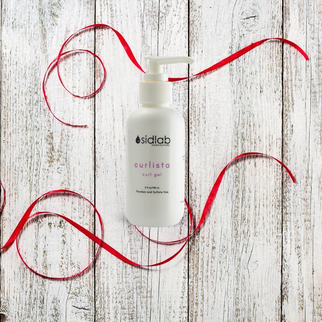 Bottle of Curlista Curl Gel on a rustic wooden surface, decorated with swirling red ribbons.