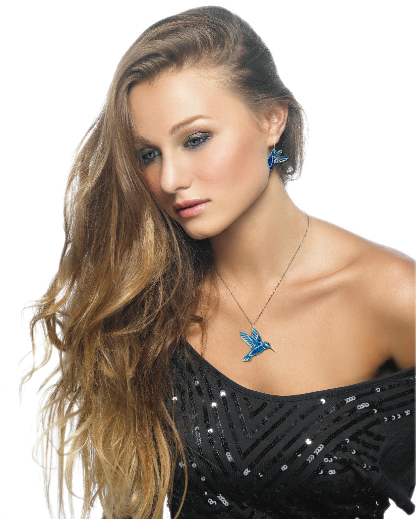A woman with long wavy hair, blue eyes, wearing 925 Sterling Silver Hummingbird Dangle Earrings and a matching necklace, posed against a white background.