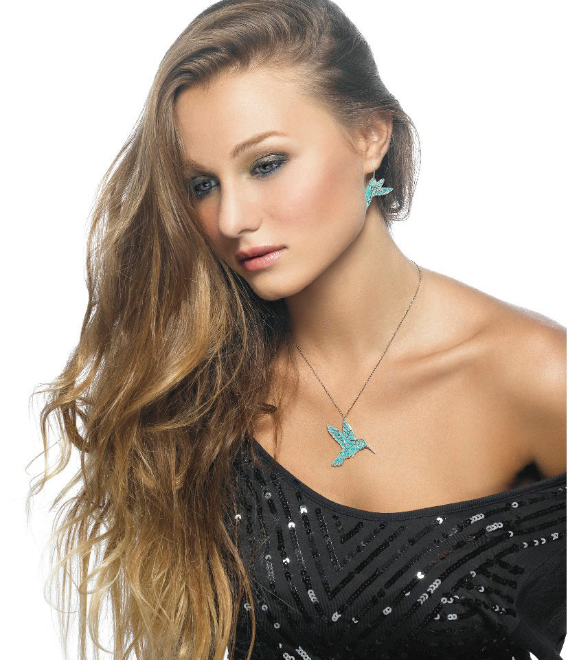 A woman with long wavy hair, blue eyes, wearing 925 Sterling Silver Hummingbird Dangle Earrings and a matching necklace, posed against a white background.